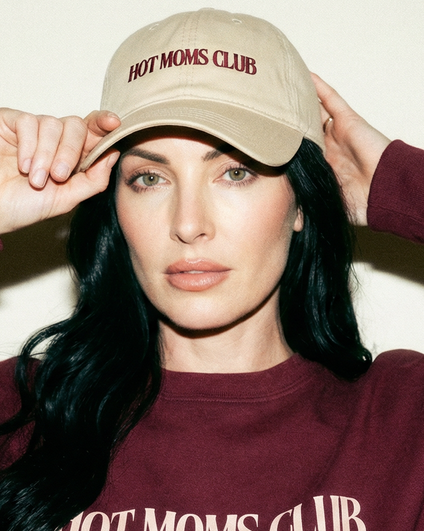 Woman wearing a beige cap and burgundy sweatshirt with 'HOT MOMS CLUB' text.