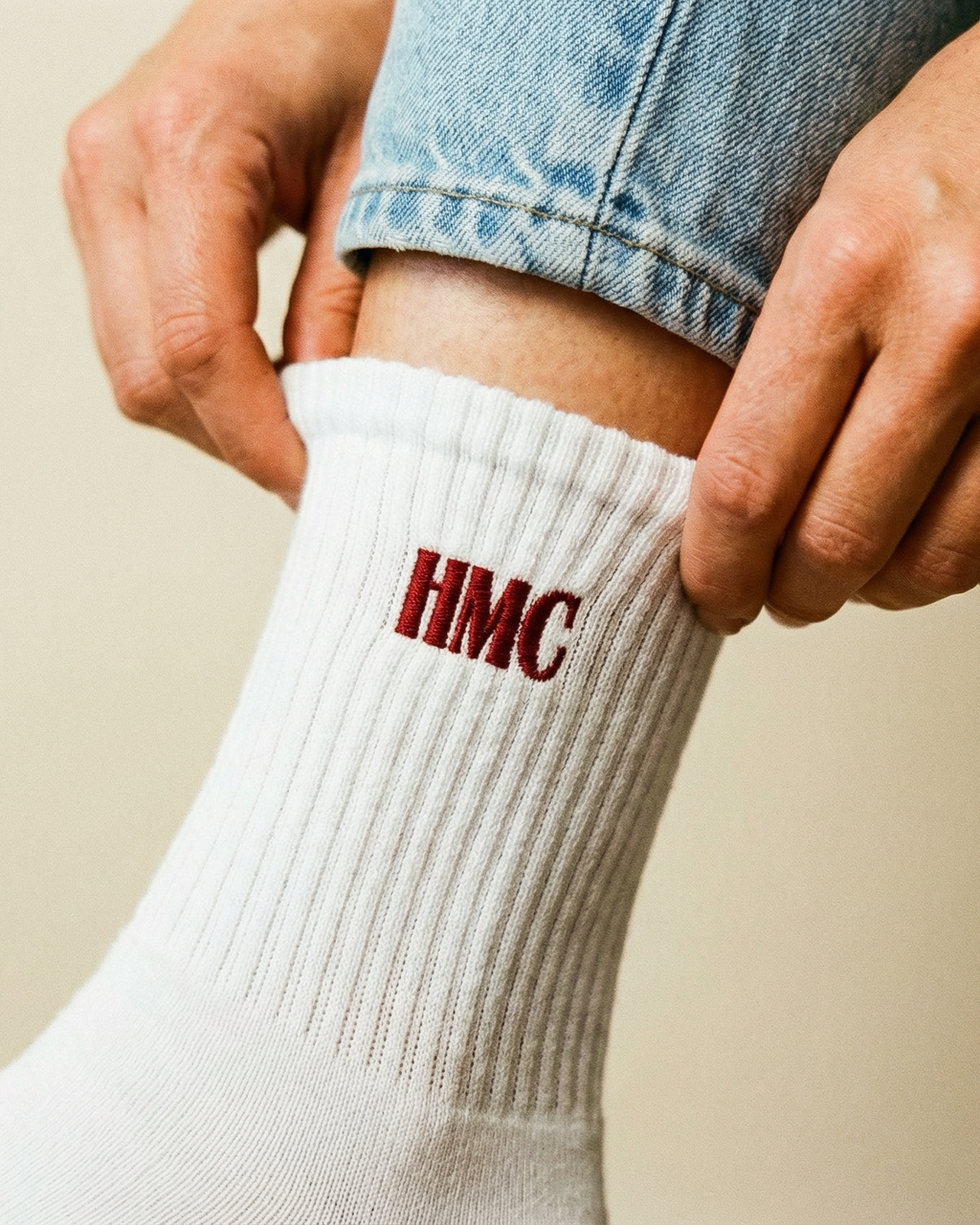 Person wearing a white sock with 'HMC' logo, holding the ankle.