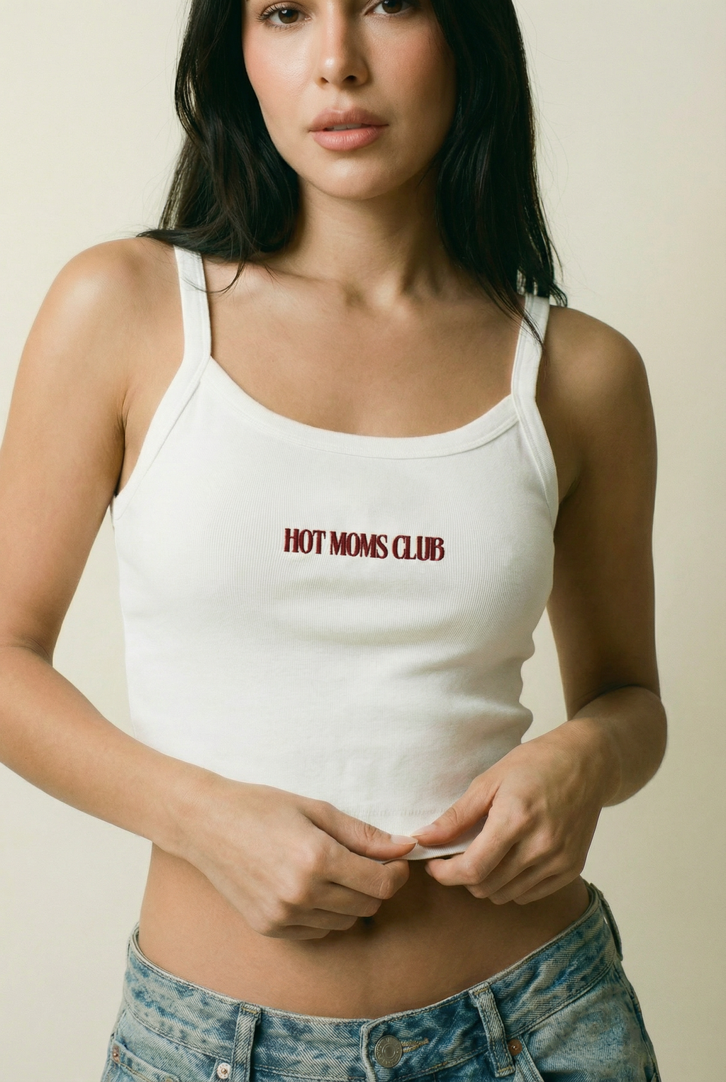 Woman wearing a white tank top with 'HOT MOMS CLUB' text against a plain background