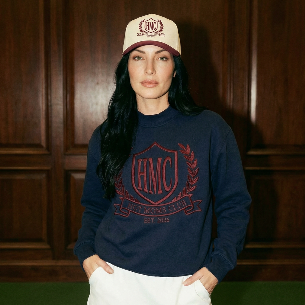 Woman wearing a navy sweatshirt with a logo and a white cap indoors.