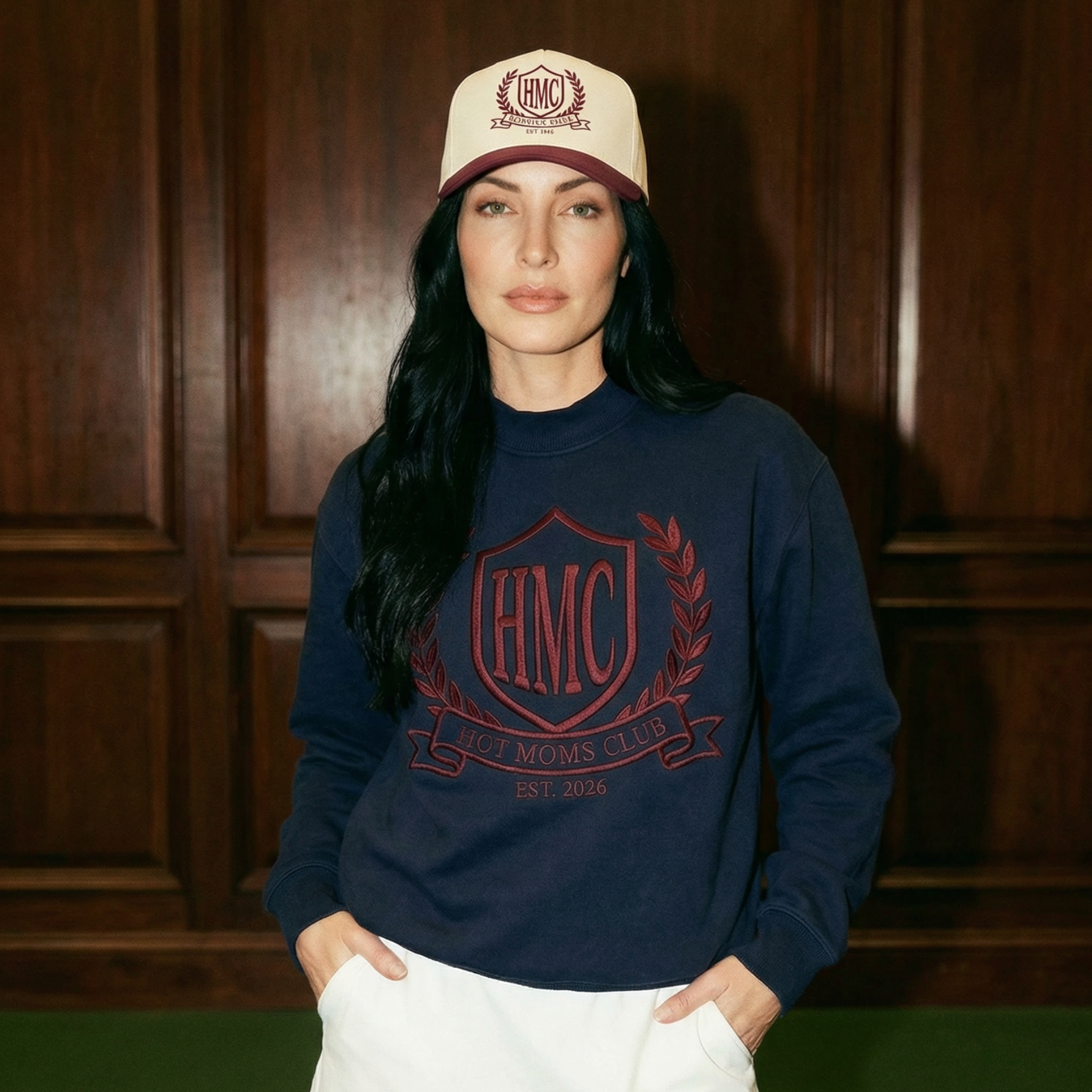 Woman wearing a navy sweatshirt with a logo and a white cap indoors.