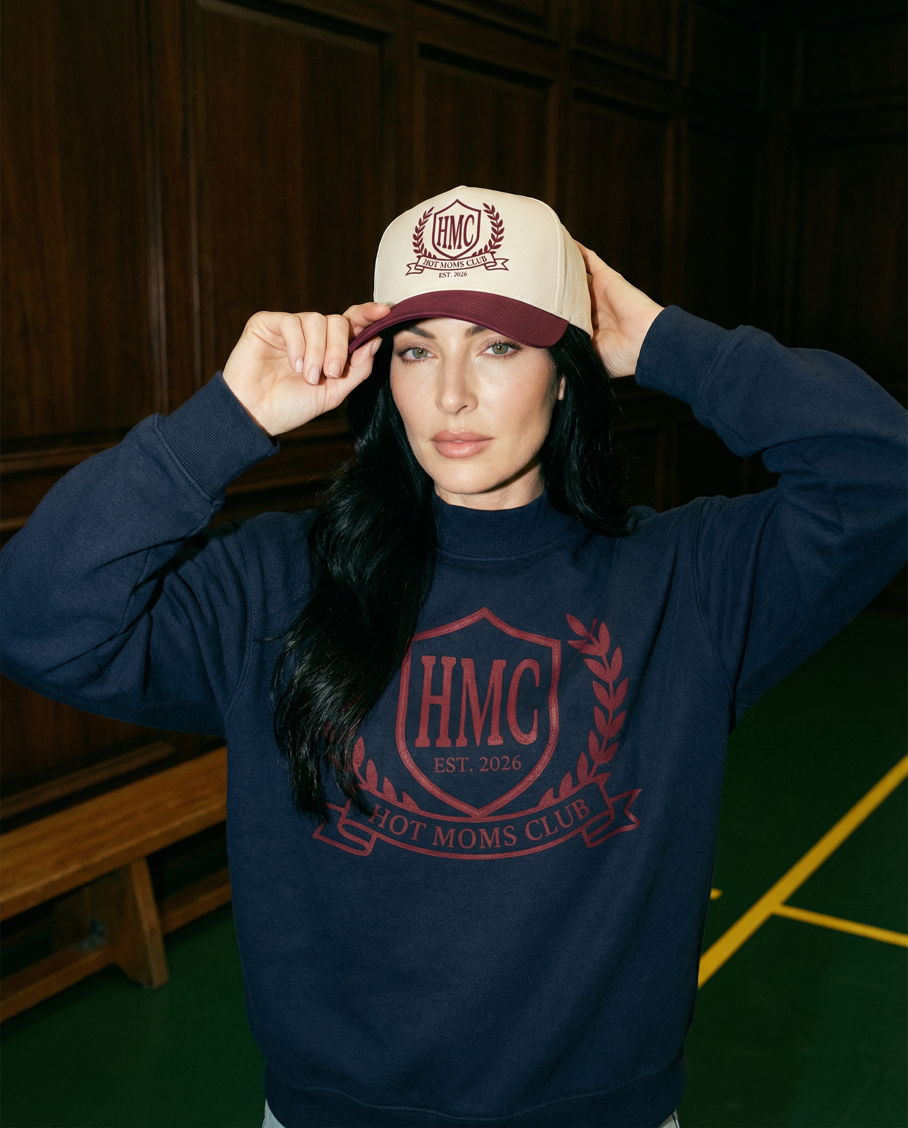 Woman wearing a navy sweatshirt with 'HMC' logo and a matching cap indoors.