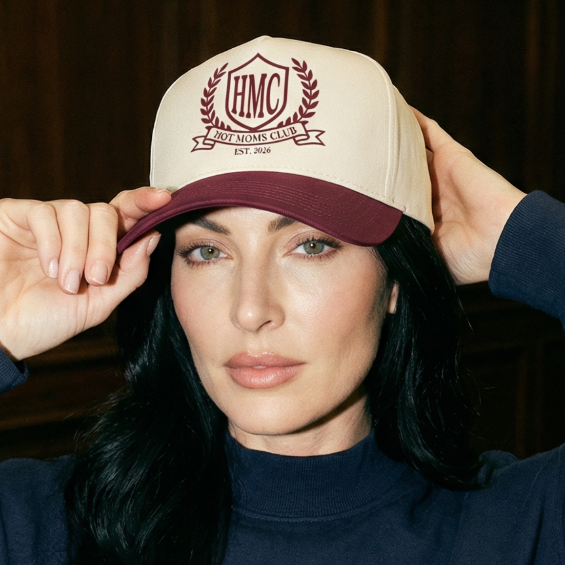 A model wearing a beige hat with maroon HMC Hot Moms Club logo embroidered