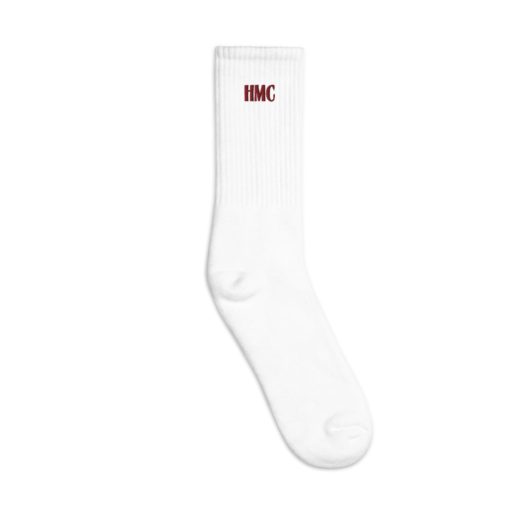 Left facing mockup of white crew socks with burgundy embroidery logo HMC