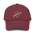 Front view of a burgundy baseball cap with "HMC" inside of a heart with an arrow through it embroidered in white thread. 