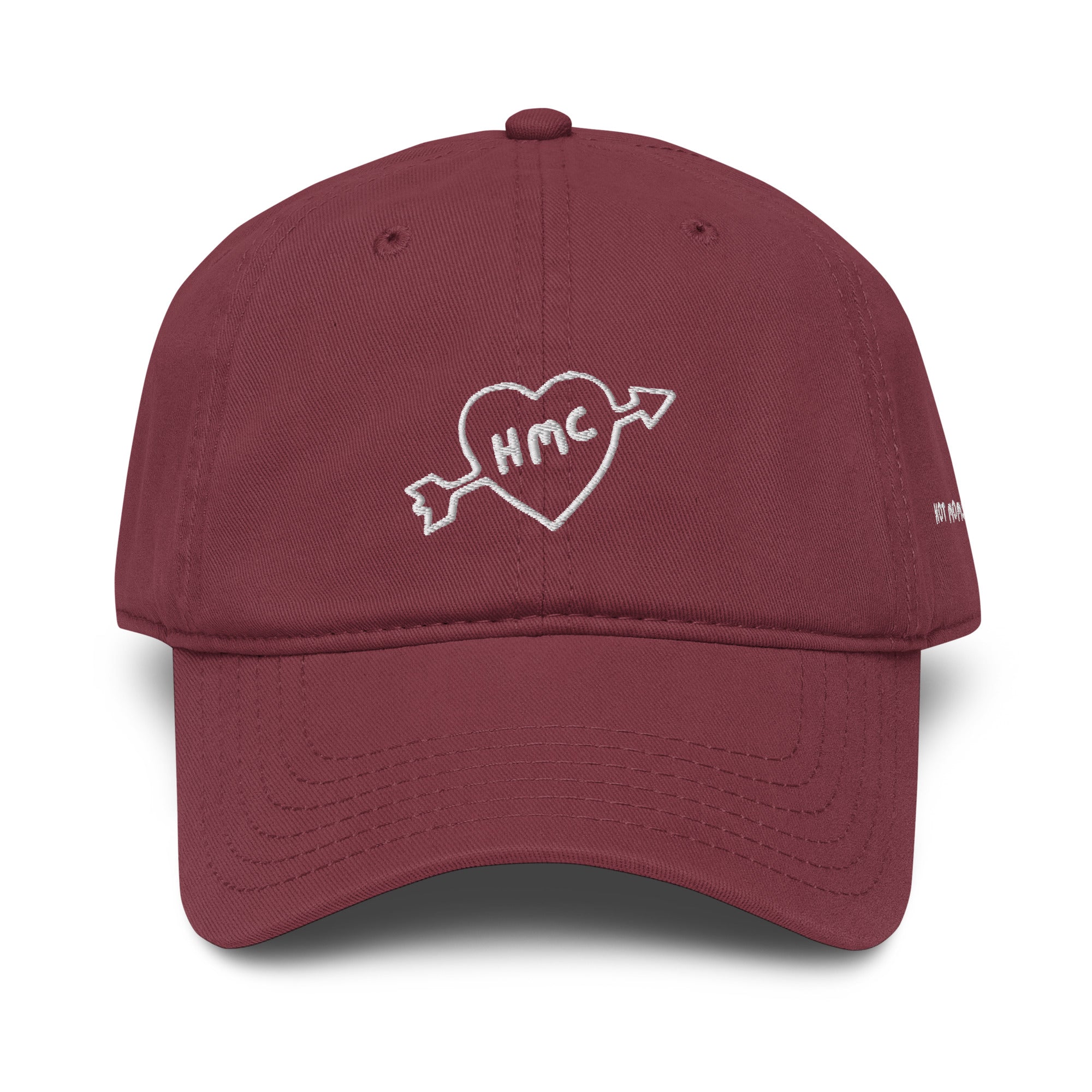 Front view of a burgundy baseball cap with "HMC" inside of a heart with an arrow through it embroidered in white thread. 